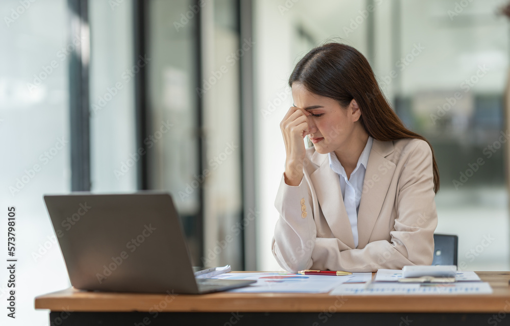 Beautiful asian businesswoman headache and stressed working in finance, management, marketing from laptop computer displaying revenue data on real estate projects in office interior. Beautiful asian businesswoman headache and stressed working in finance, management, marketing from laptop computer displaying revenue data on real estate projects in office interior.