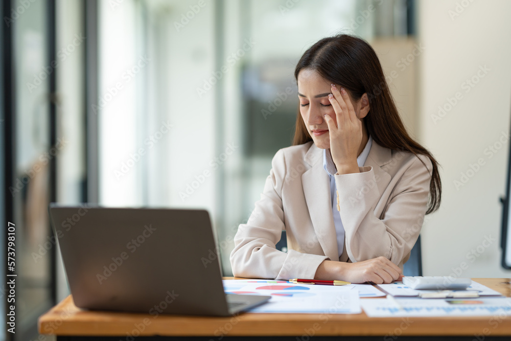Beautiful asian businesswoman headache and stressed working in finance, management, marketing from laptop computer displaying revenue data on real estate projects in office interior. Beautiful asian businesswoman headache and stressed working in finance, management, marketing from laptop computer displaying revenue data on real estate projects in office interior.