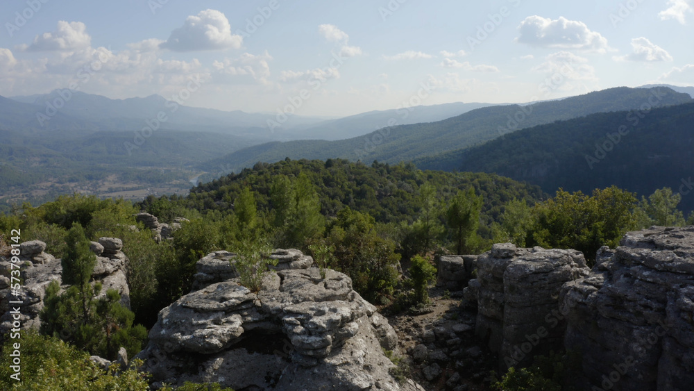 Top view of beautiful grey rock formations among green trees. Panoramic aerial view of mountains and sky on a summer day.
