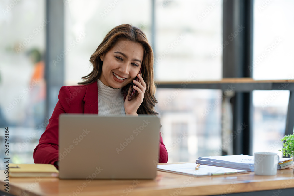Beautiful asian businesswoman working with laptop computer is using mobile phone for talking. Finance business contacts in real estate projects in her office. Beautiful asian businesswoman working with laptop computer is using mobile phone for talking. Finance business contacts in real estate projects in her office.