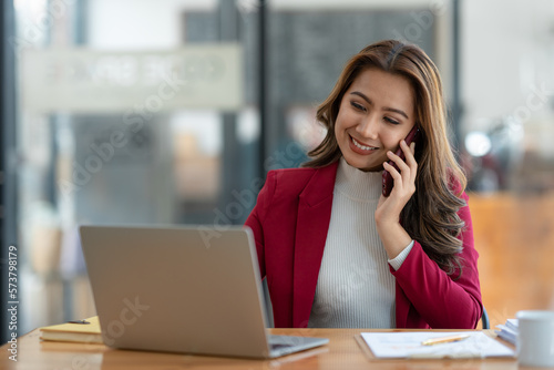Beautiful asian businesswoman working with laptop computer is using mobile phone for talking. Finance business contacts in real estate projects in her office.