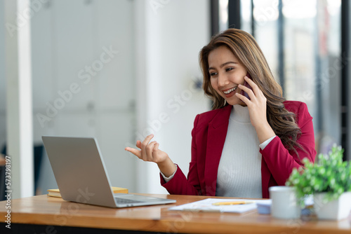 Beautiful asian businesswoman working with laptop computer is using mobile phone for talking. Finance business contacts in real estate projects in her office.