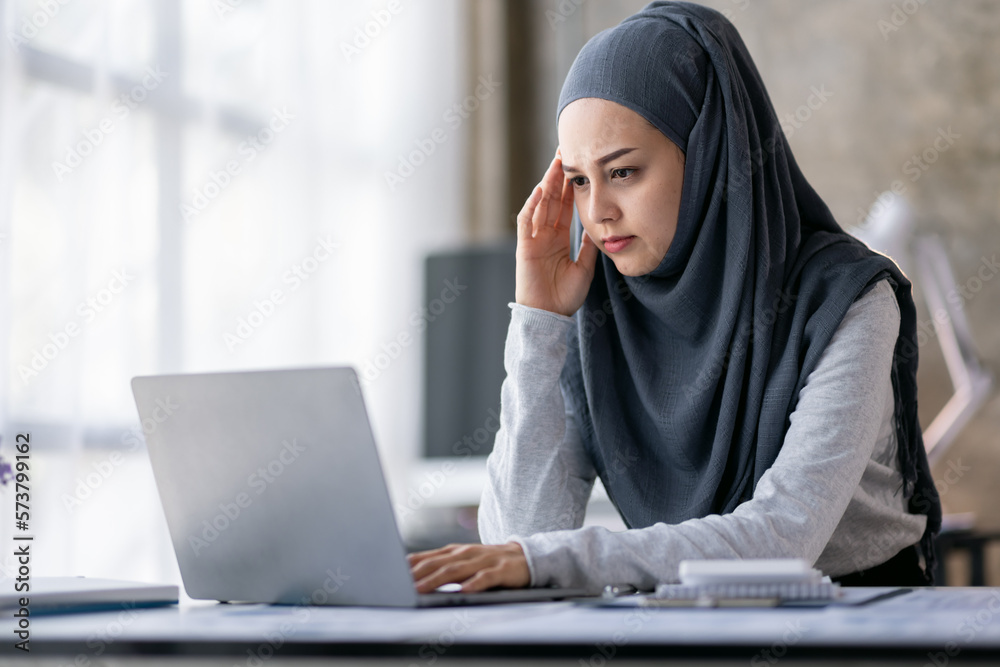 Portrait of tired young business Asian muslim woman work with documents tax laptop computer in office. Sad, unhappy, Worried, Depression, or employee life stress concept Portrait of tired young business Asian muslim woman work with documents tax laptop computer in office. Sad, unhappy, Worried, Depression, or employee life stress concept