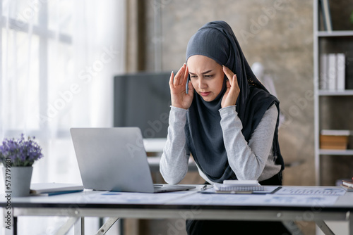 Portrait of tired young business Asian muslim woman work with documents tax laptop computer in office. Sad, unhappy, Worried, Depression, or employee life stress concept 