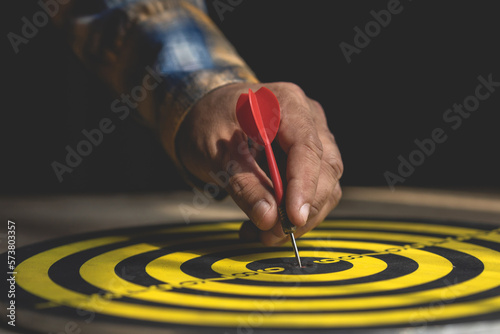 Businessman working in the office and point in the center of yellow dartboard. Goal and success for business concept.