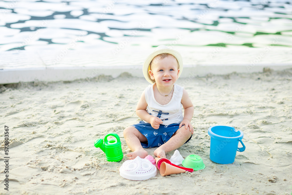 a baby boy of six months plays in the sand with toys on the embankment by the water of the sea, the concept of recreation and travel a baby boy of six months plays in the sand with toys on the embankment by the water of the sea, the concept of recreation and travel