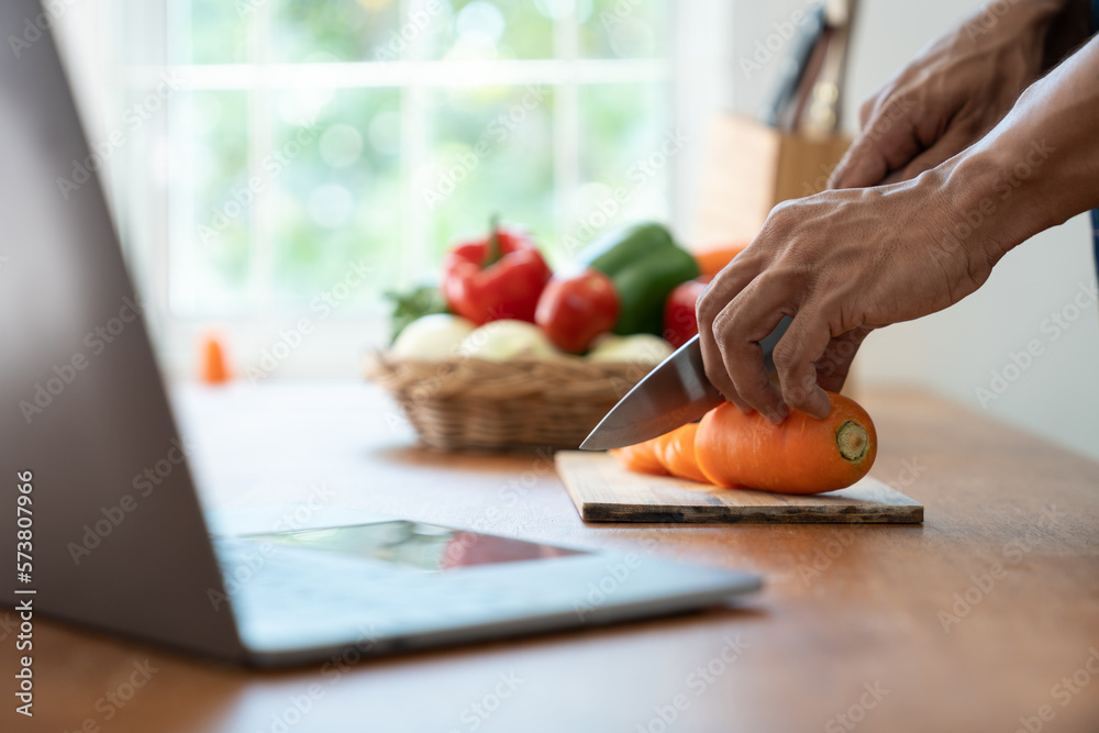Asian strong man Wearing an apron having fun while preparing ingredients such as fruits and vegetables. learn how to do Chopping Carrots via Application Happily online in the kitchen. Asian strong man Wearing an apron having fun while preparing ingredients such as fruits and vegetables. learn how to do Chopping Carrots via Application Happily online in the kitchen.