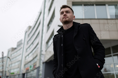 stylish brutal man in a black coat on the background of city buildings