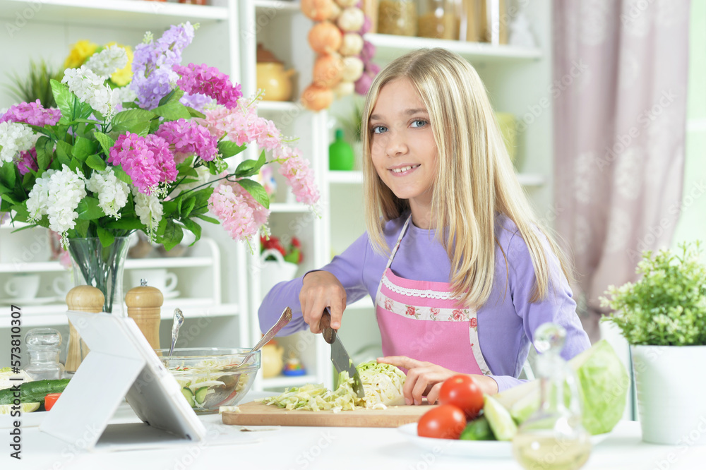 girl preparing fresh salad on kitchen table with tablet at home girl preparing fresh salad on kitchen table with tablet at home
