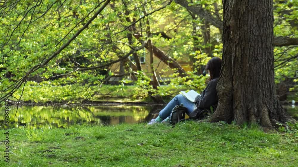 Attractive young woman reading book while sitting on grass in green public park. Springtime outdoors. Greenery unity with nature. Spend free time on open air. 4k Education concept Attractive young woman reading book while sitting on grass in green public park. Springtime outdoors. Greenery unity with nature. Spend free time on open air. 4k Education concept