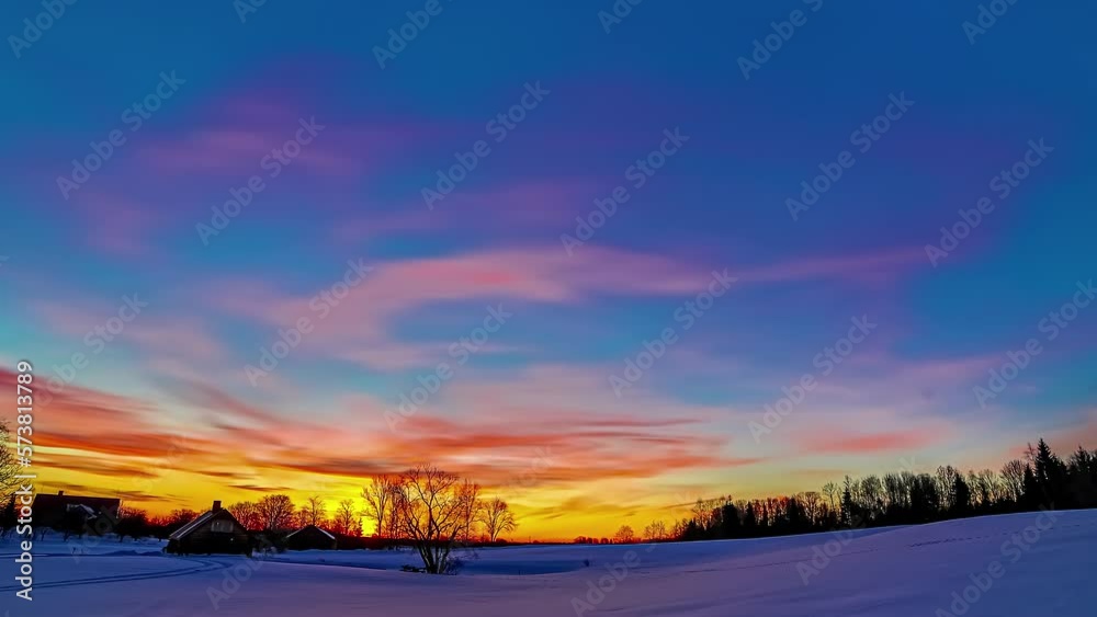 Timelapse of a snowy landscape with trees under a cloudy yellow and blue sky at sunset. Timelapse of a snowy landscape with trees under a cloudy yellow and blue sky at sunset.