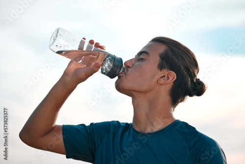 Fitness, drinking water and man with training, exercise and workout for balance, healthy lifestyle and thirsty. Male, athlete and runner with liquid, aqua and hydration after practice, sunset and sky