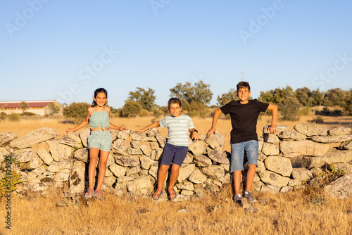 Three kids in front of a stone wall at summer