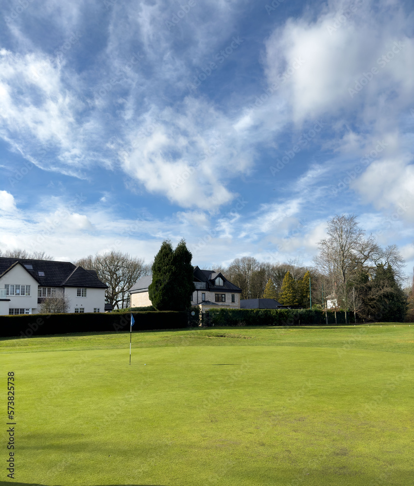 Flag and the hole at golf club The Mere Cheshire, blue sky summers day with some clouds. Large surrounding houses Flag and the hole at golf club The Mere Cheshire, blue sky summers day with some clouds. Large surrounding houses