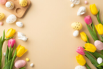 Easter decorations concept. Top view photo of colorful easter eggs ceramic easter bunnies yellow and pink tulips and wooden egg holder on isolated pastel beige background with empty space