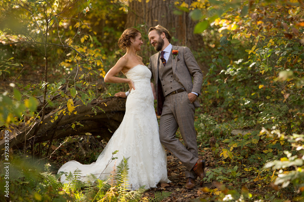 Bearded groom in grey suit and bride in wedding dress looking into each other’s eyes in the foliage of a forest Bearded groom in grey suit and bride in wedding dress looking into each other’s eyes in the foliage of a forest
