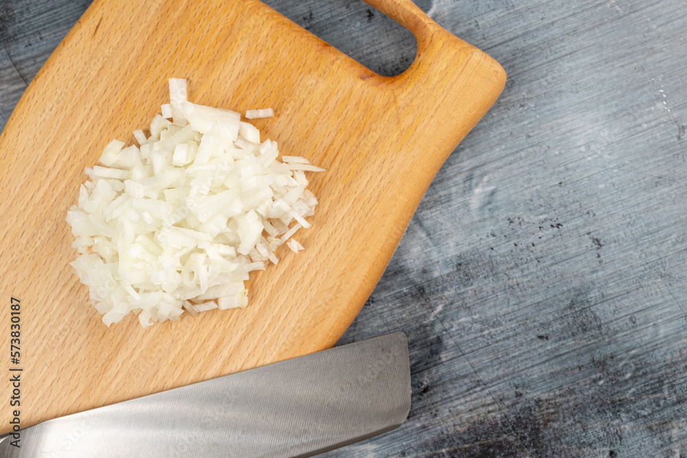 Chopped onions on the wooden board above blue dark moody background