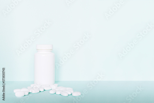 white pills and a plastic container on a blue background. Medical theme. 