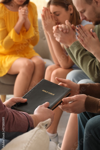 Group of people praying with Holy Bible at home  closeup