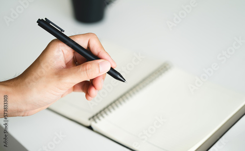 left handed man holding a pen and writing in a notebook on the table