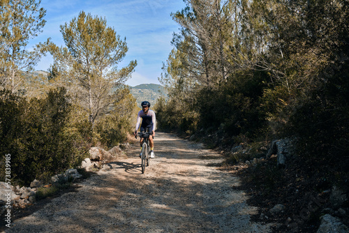 Fit male cyclist riding dirt trails on a gravel bike. A man riding a gravel bike on a gravel road in a scenic view with hills in Alicante region, Spain. Sports motivation.Gravel road in mountains.