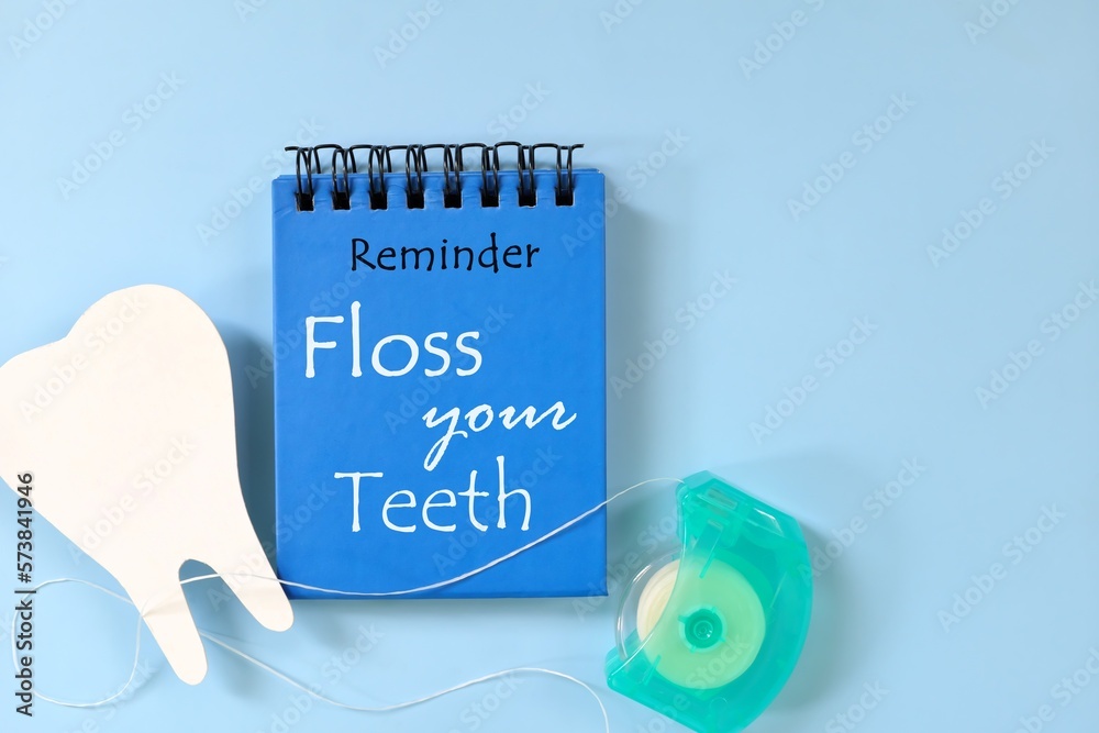 Floss your teeth reminder on blue notepad. Dental and oral health care concept.