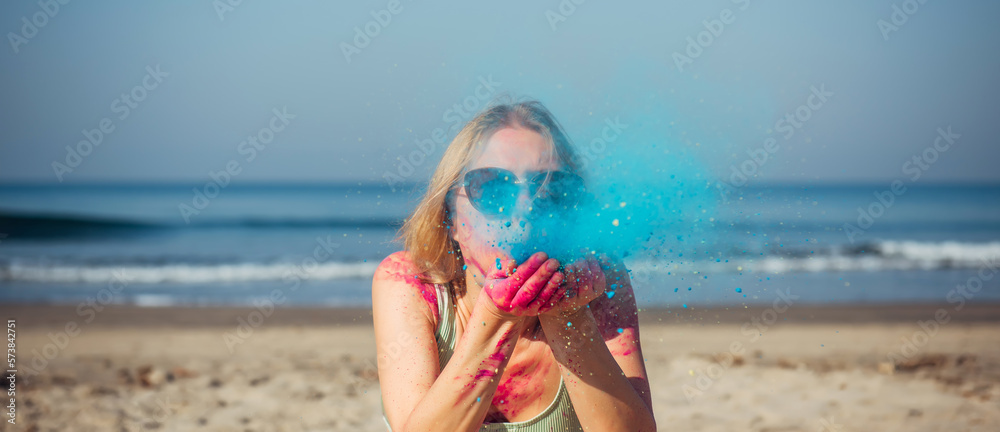 A beautiful girl on the seashore in a multicolored Holi powder smiles and waves her hands at the Holi Festival. Tourist trips to India for the Happy Holi Festival