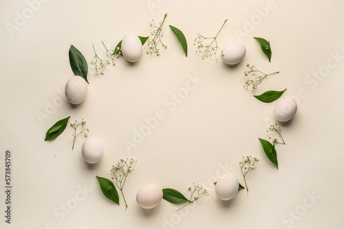 Frame made of Easter eggs, green leaves and gypsophila flowers on white background