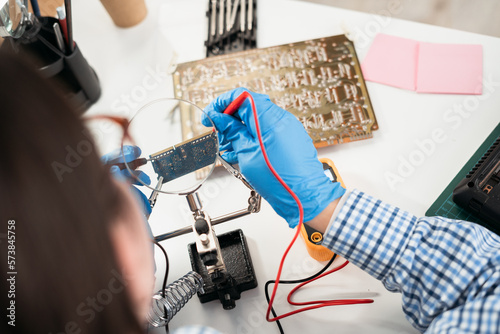 Measurement with a multimeter of resistance in the computer board. Checking circuit board with multimeter on the wooden table at computer service