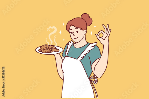 Smiling housewife in kitchen apron preparing homemade cookies to invite family for breakfast. Positive housewife learns how to cook desserts and pastries, wanting to surprise husband and children 