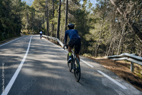  A group of young cyclist rides bikes on a road in mountain forest.Close up back view of a young fit strong fast cyclists during ride. Calp, Alicante, Spain