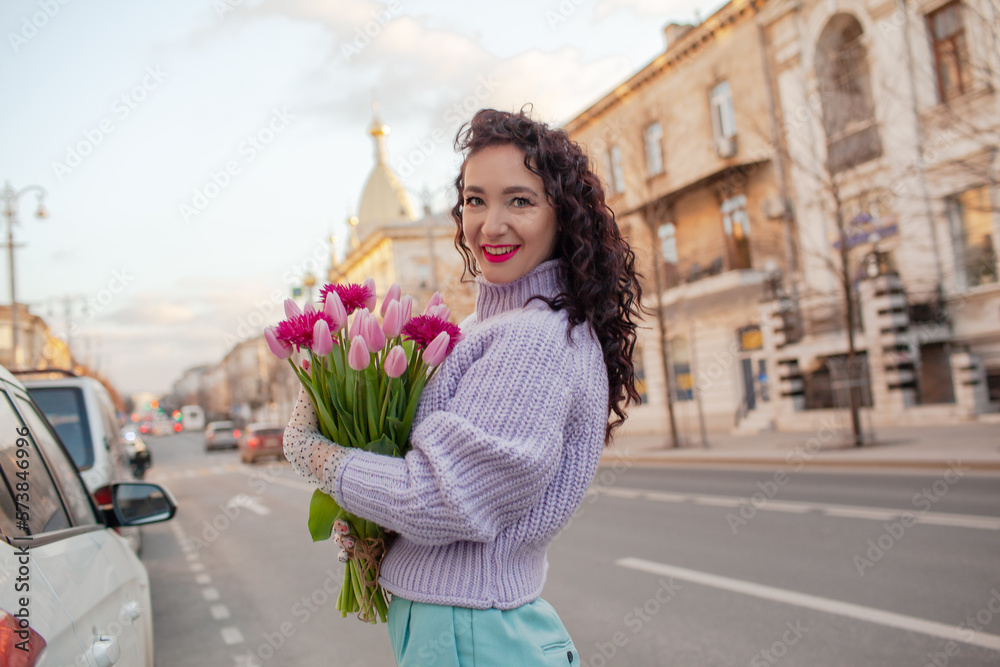 Fototapeta premium 35 years old woman is walking with a bouquet of flowers in the spring streets of the city