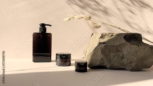 Set of amber jars with cream or lotion on a beige background in the morning rays of the sun with a flower shadow.