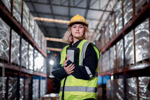 Worker industry warehouse in helmets woman order details and checking goods and supplies on shelves with goods background in warehouse is industry logistic and business export concept.