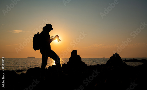 Silhouette photographer take photo on stone near beach on vacation day with sun sky background.