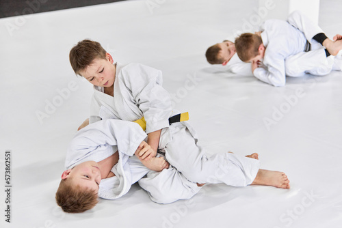 Boys, children in white kimono training, practising judo, jiu-jitsu exercises indoors. Competition. Strength. Concept of martial arts, combat sport, sport education, childhood, hobby