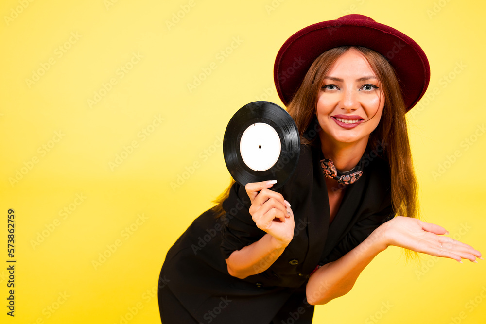 Obraz premium girl in a black suit on a yellow background with a record in her hands, music, the girl shows emotions