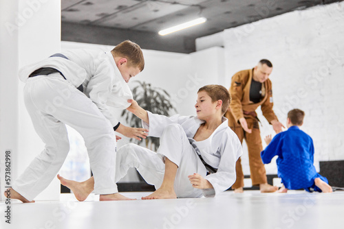 Professional sport activity. Boys, children in white kimono training, practising judo, jiu-jitsu exercises indoors. Concept of martial arts, combat sport, sport education, childhood photo