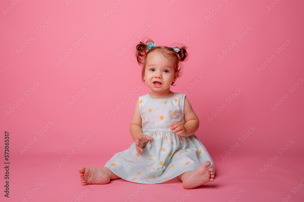 baby girl in a beautiful dress sitting on a pink background