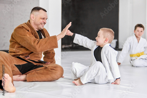 Cooperation. Friendly man, judo, jiu-jitsu coach training with little boys, children. Teaching fight exercises. Concept of martial arts, combat sport, sport education, childhood, hobby photo