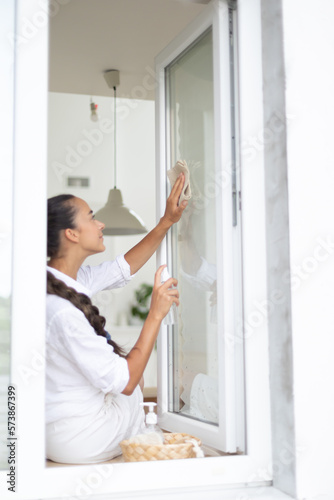 Woman cleaning window at home with rag and spray.