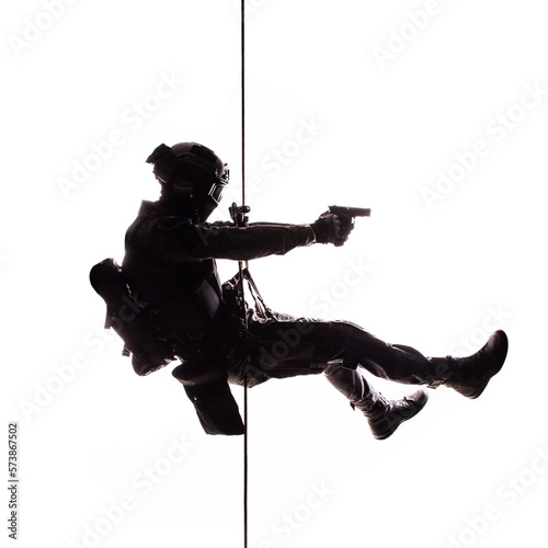 Silhouette of police officer in tactical gear descending from a height, rope exercises with weapons. Tactical rappelling, anti-terror or counter terrorism operation in darkness in rappelling harness