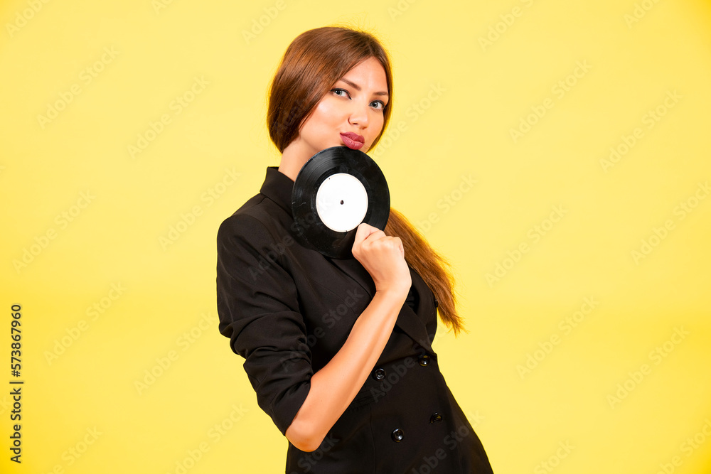 Fototapeta premium girl in a black suit on a yellow background with a record in her hands, music, the girl shows emotions