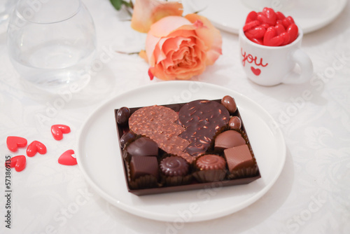 Close up of dark and milk chocolate with almond in a heart shape in a plate with little mini heart and mug wrote with letter "you" and orange color rose in background with cozy ambiance of lovers