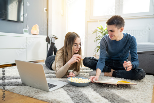 Beautiful young teenage couple sitting on the floor, eating popcorn and studying together at home.