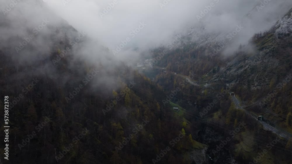 Relaxed Forward flying drone video towards clouds in Swiss Alps valley on moody grey winter afternoon with lush pine forests and beautiful snowy trees on mountains with road down middle of the valley Relaxed Forward flying drone video towards clouds in Swiss Alps valley on moody grey winter afternoon with lush pine forests and beautiful snowy trees on mountains with road down middle of the valley