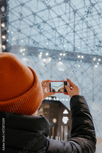 Young woman taking a photo. Inverted pyramid in the shopping mall 'Carrousel du Louvre' with people in Paris, France. Louvre museum hosts one of the biggest art collection in the world. photo