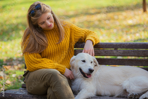 Belgrade, Serbia. November 10th, 2022. Beautiful young woman petting her cute golden retriever sitting on a park bench on a sunny day.