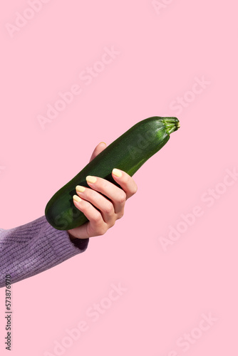 Woman's hand holding ripe green zucchini on pink background, minimal style, copy space