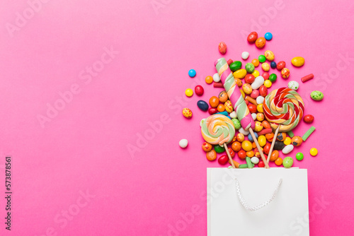shopping paper gift bag in corner full of assorted traditional candies falling out on colored background with copy space. Happy Holidays sale concept
